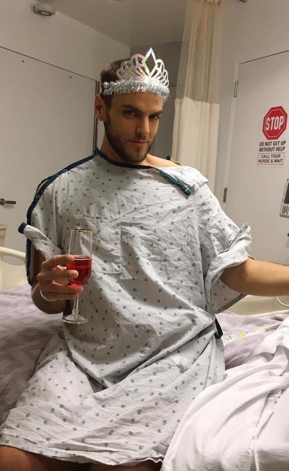 Rob in a hospital gown wearing a tiara and raising a juice cup