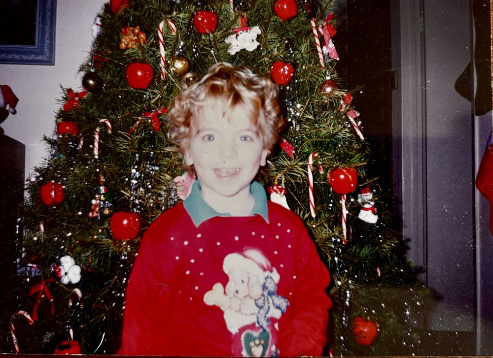 Rob as a kid in a red sweater in front of a Christmas tree